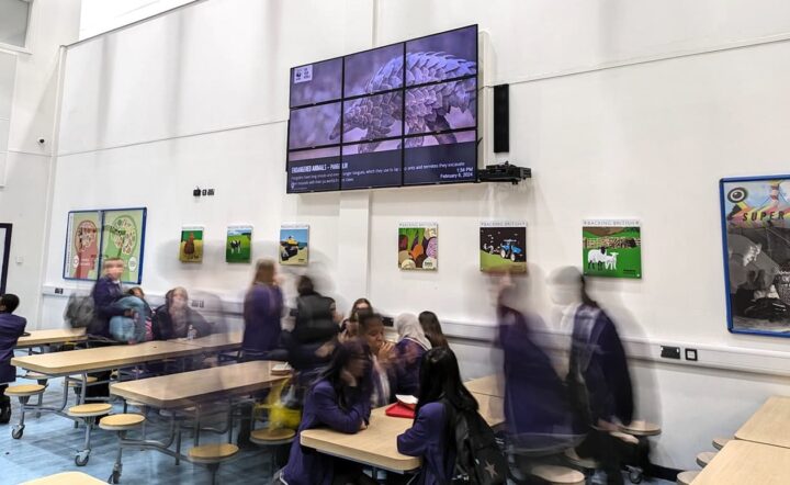 School cafeteria with students and a large digital signage display.