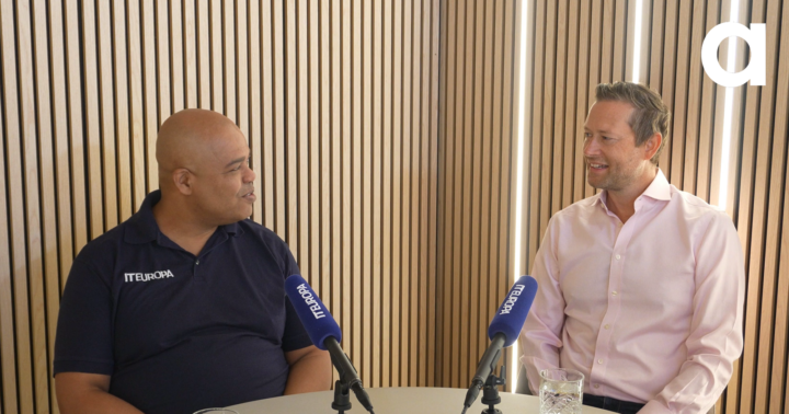 Two people sat at a table with microphones during a recorded interview.